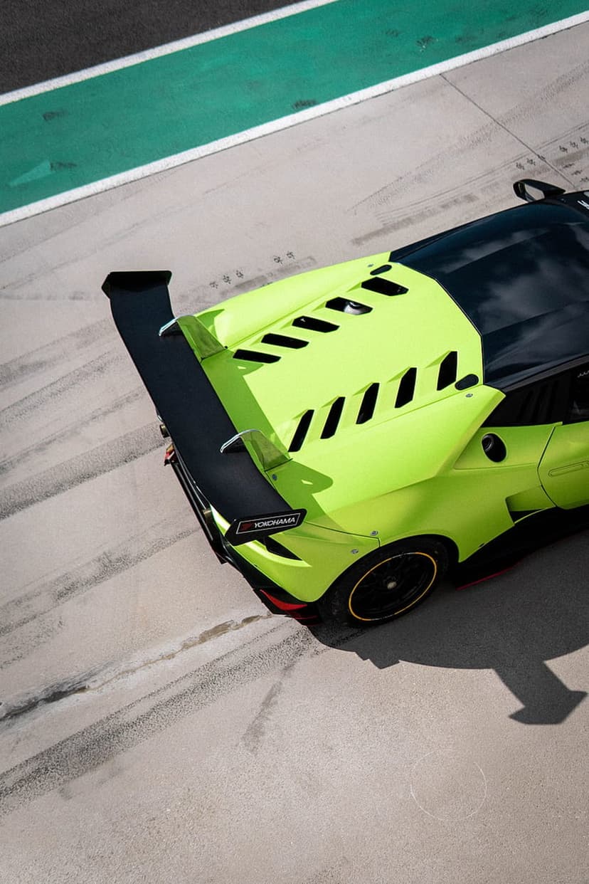 Lime green Lamborghini race car with a black rear wing maneuvers along a grey track with green racing lines.