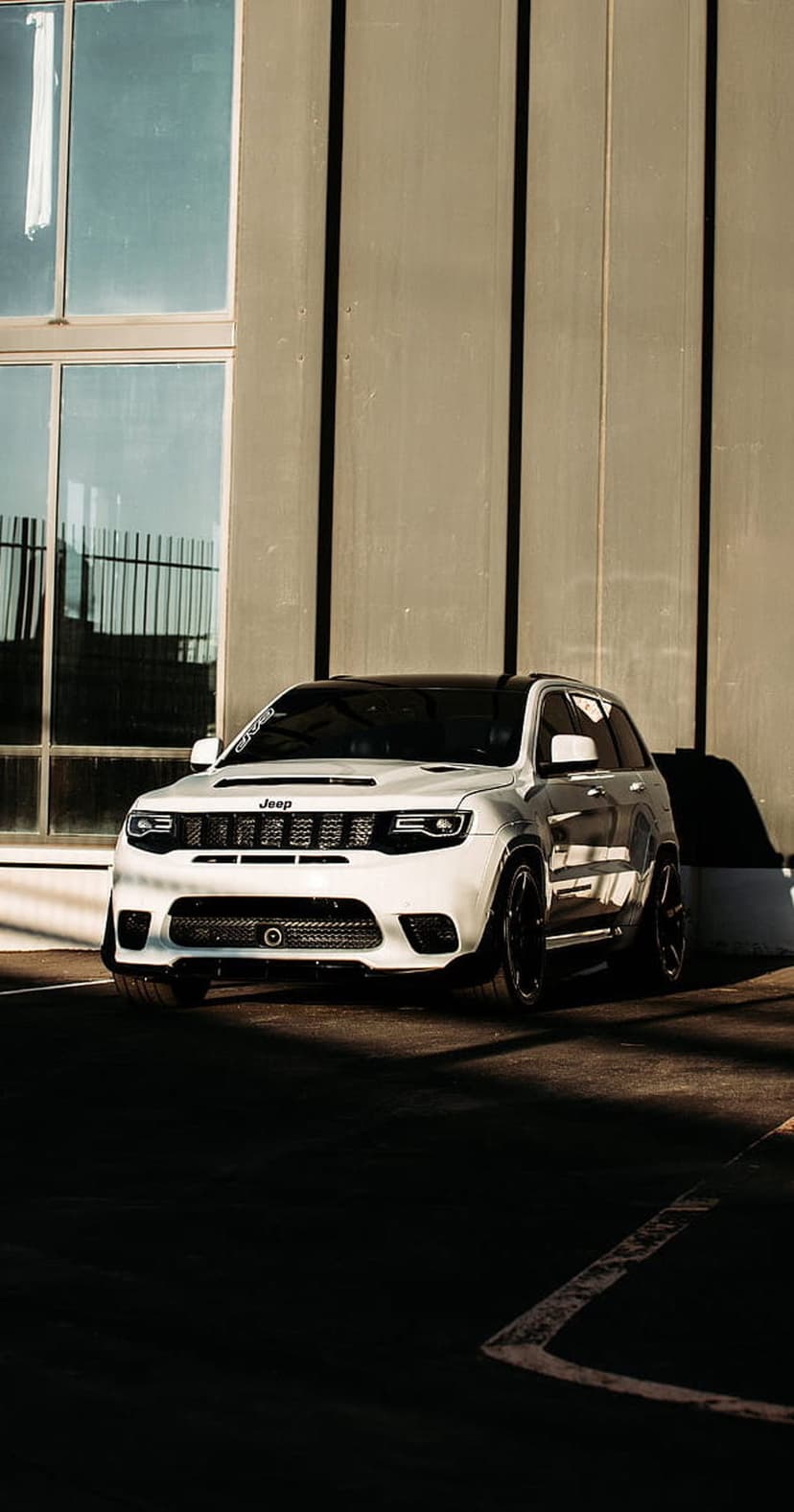 White Jeep Grand Cherokee SRT parked in front of a modern building with large glass windows and dramatic shadows.