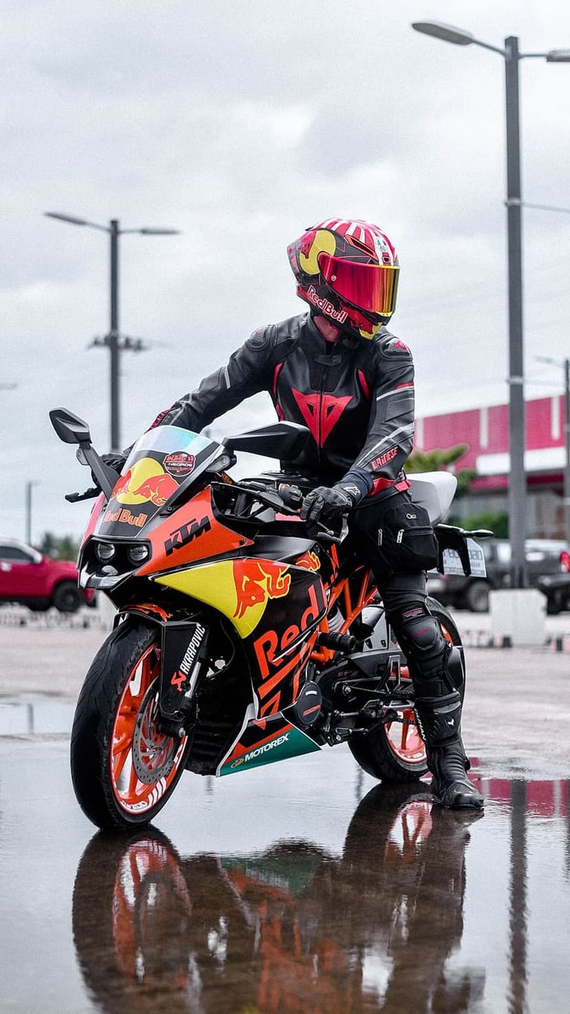 Red Bull KTM rider on an orange motorcycle sits on wet pavement with clear reflections on the ground.