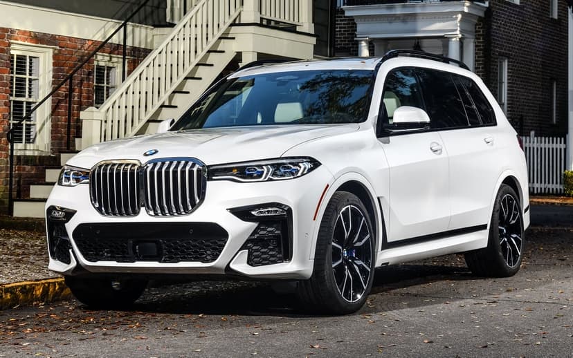 Front view of a white BMW X7 SUV parked on a suburban street with a brick house and white stairs behind.