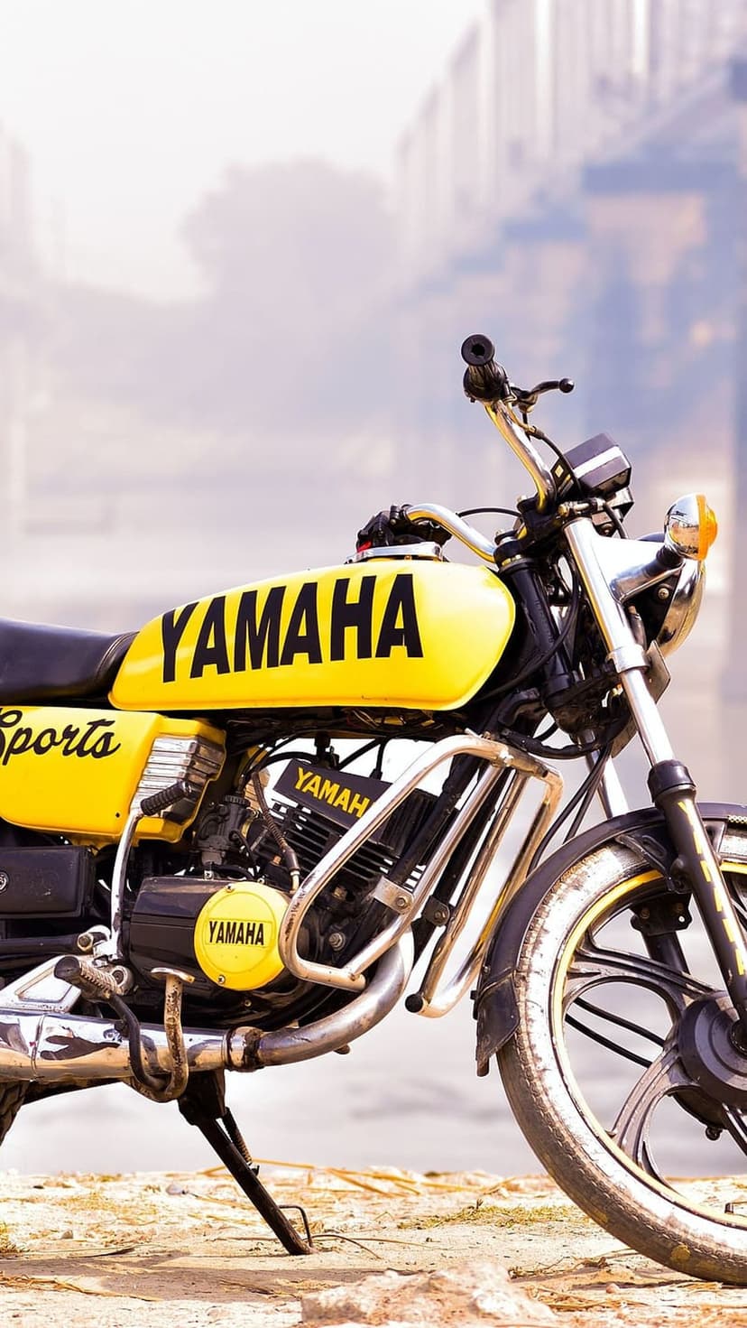 Yellow Yamaha motorcycle fuel tank and engine block shown in a close-up shot with a blurred urban background.