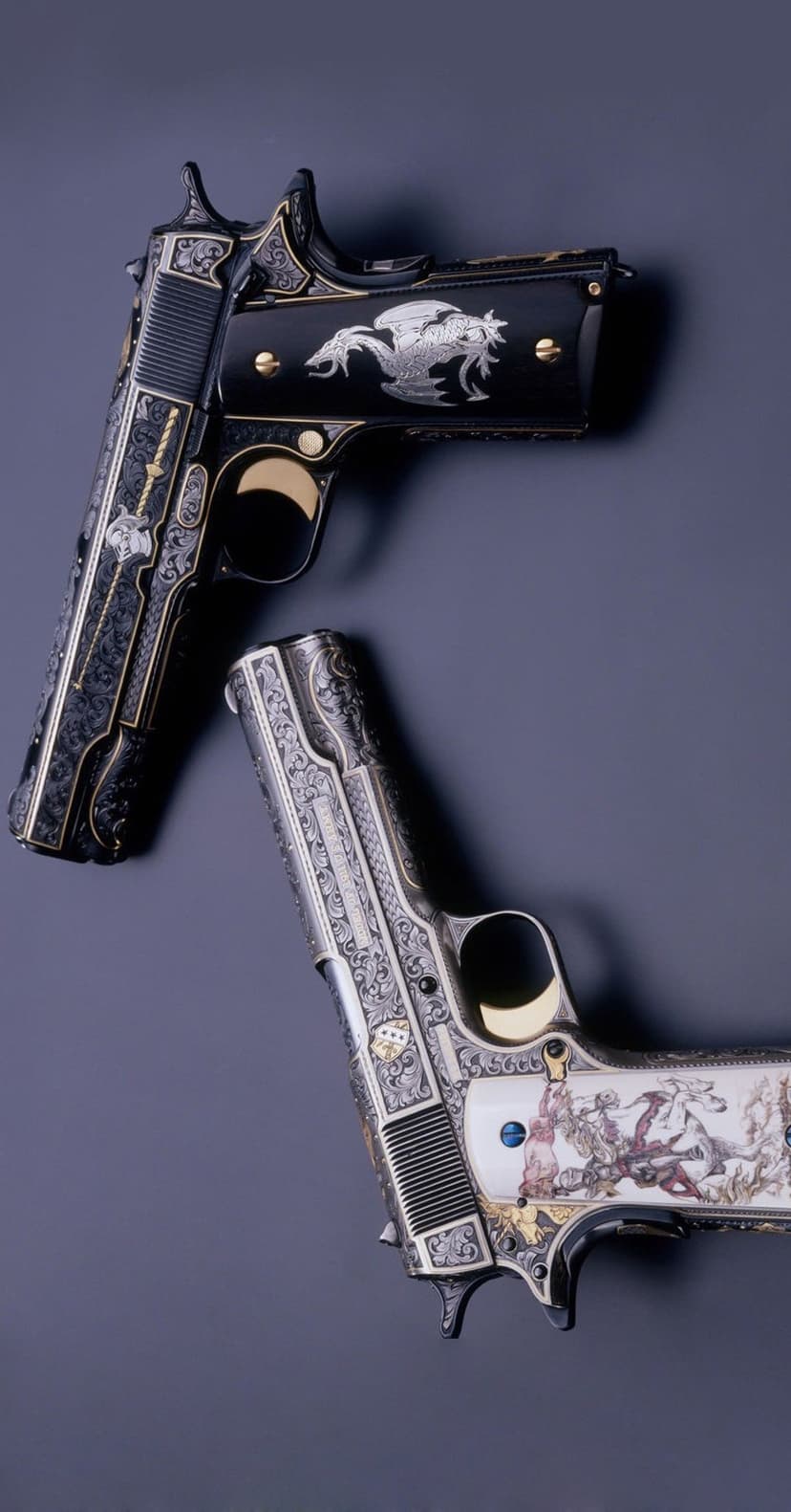 Pair of engraved Colt 1911 pistols with silver dragon motifs and gold battle scenes on a dark studio backdrop.