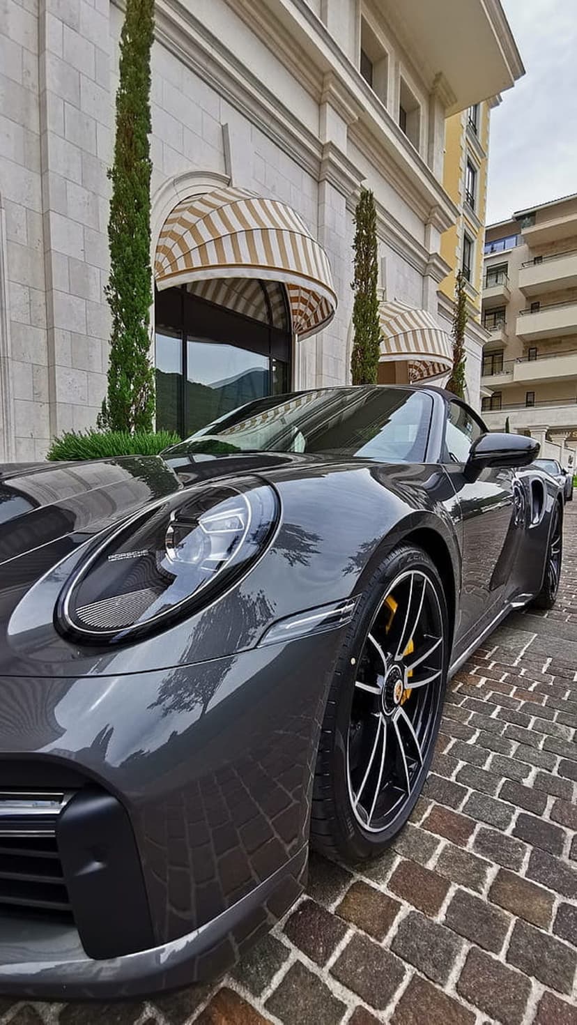 Dark gray Porsche convertible parked on a cobblestone street in front of a building with striped awnings.