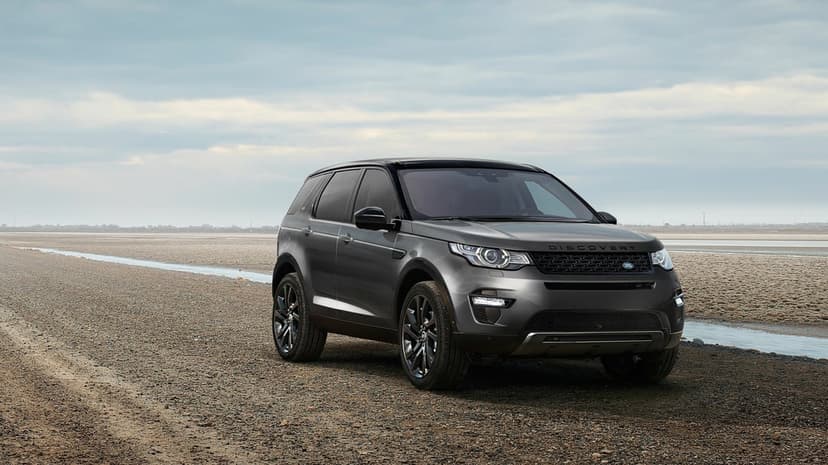 Dark grey SUV parked on a vast gravel plain under a cloudy sky with a small stream in the background.