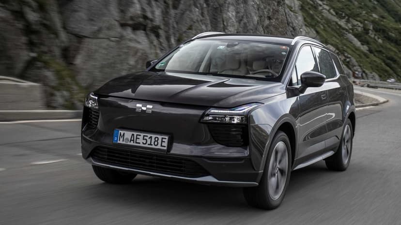 Dark grey electric SUV driving on a winding mountain road with rocky cliffs and motion blurred asphalt.