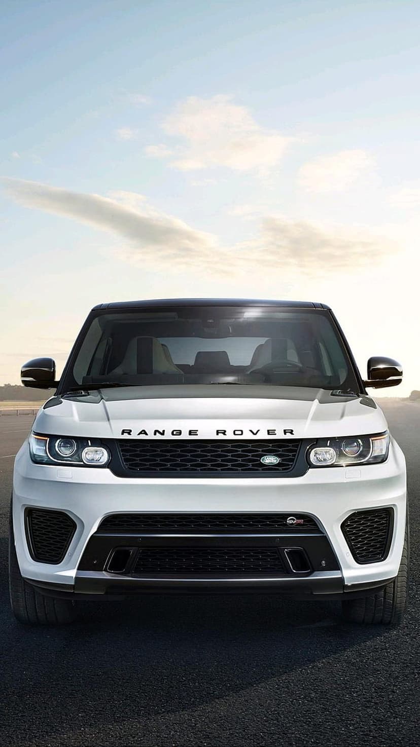 White Range Rover Sport SVR with a black grille and sharp headlights parked on asphalt under a cloudy sky.