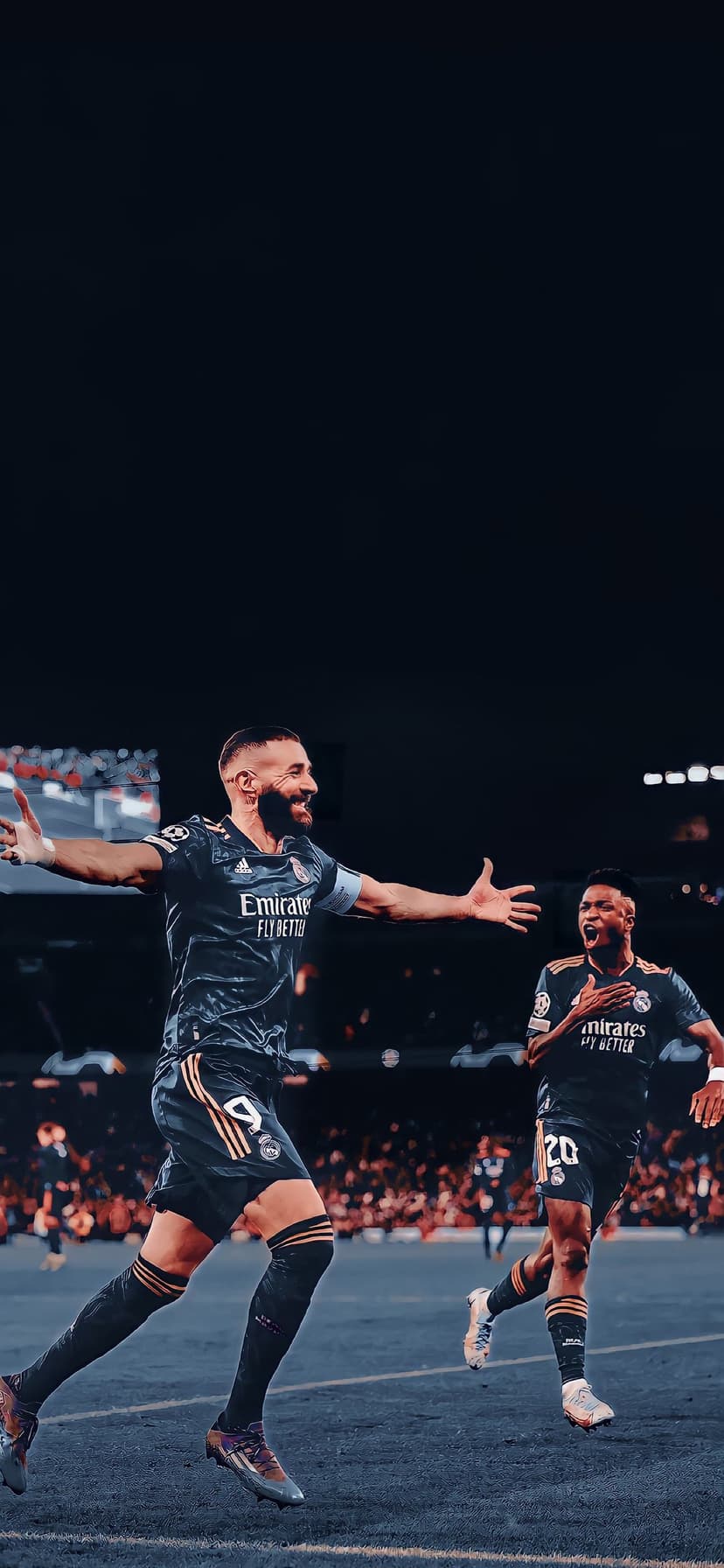 Karim Benzema and Vinicius Junior celebrate a goal on a grass pitch wearing dark blue Real Madrid football kits.