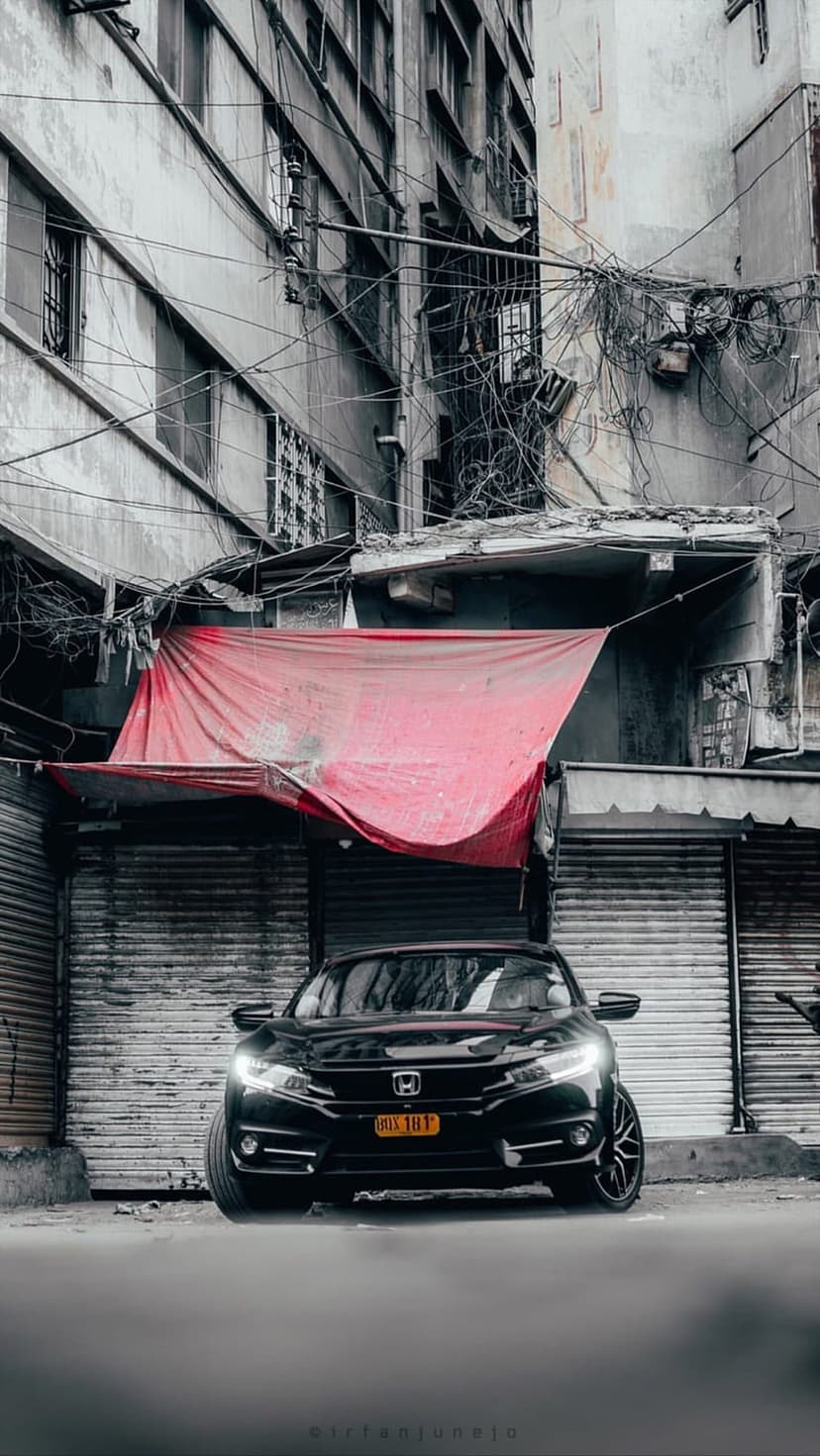 Black Honda Civic parked in a dark alleyway with weathered brick walls, hanging wires, and a red tarp.