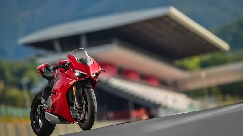 Red Ducati Panigale V4 motorcycle on a race track with a blurred grandstand and mountain background.
