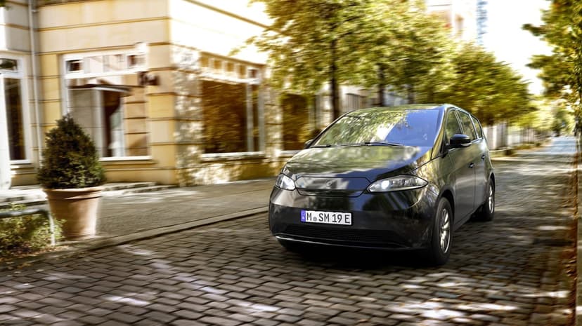 Black solar electric car driving on a cobblestone city street with motion-blurred trees and buildings.