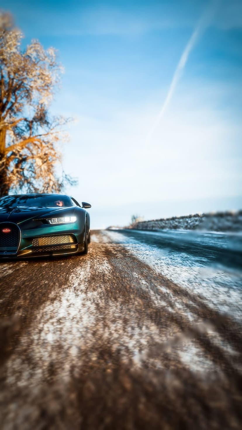 Bugatti Chiron hypercar driving on a snowy road past a bare tree under a clear blue winter sky at a low angle.