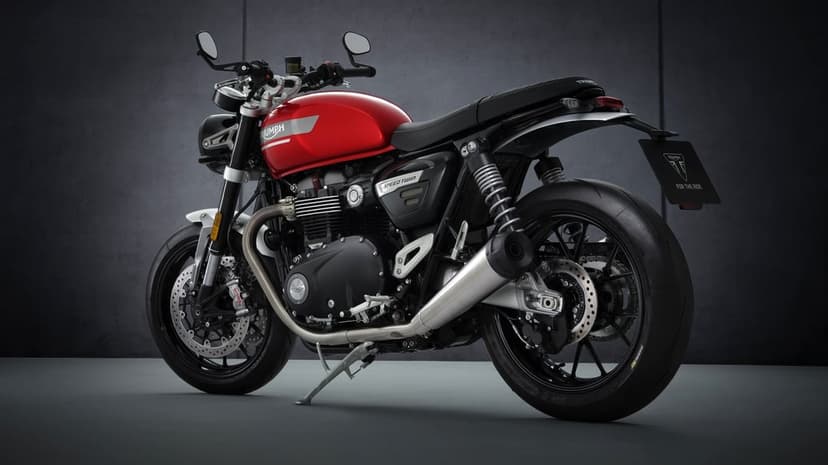 Red Triumph Speed Twin motorcycle with black engine and silver exhaust against a dark textured studio wall.