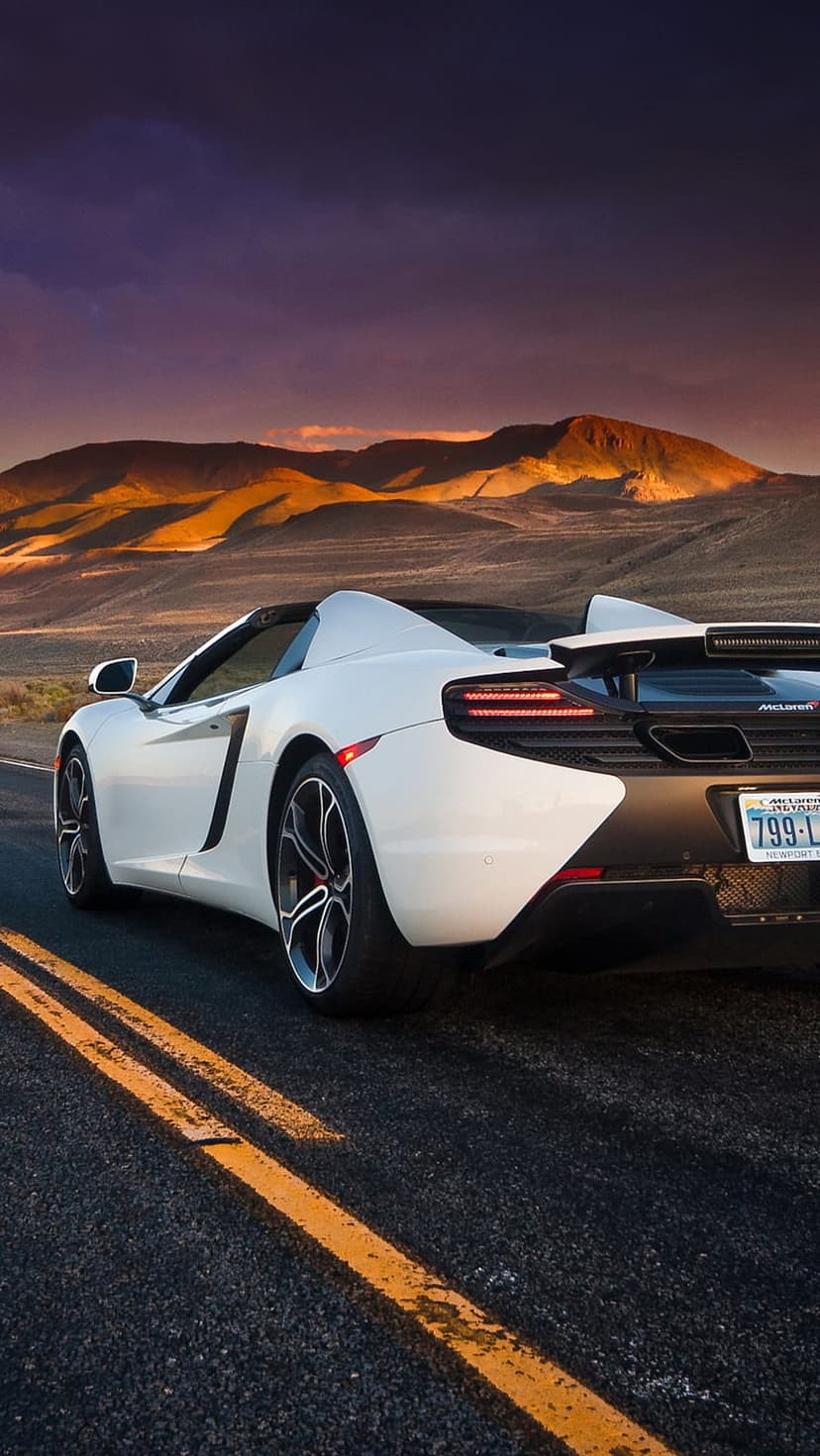 White McLaren supercar driving on a desert highway under a purple sunset sky with visible glowing red taillights.