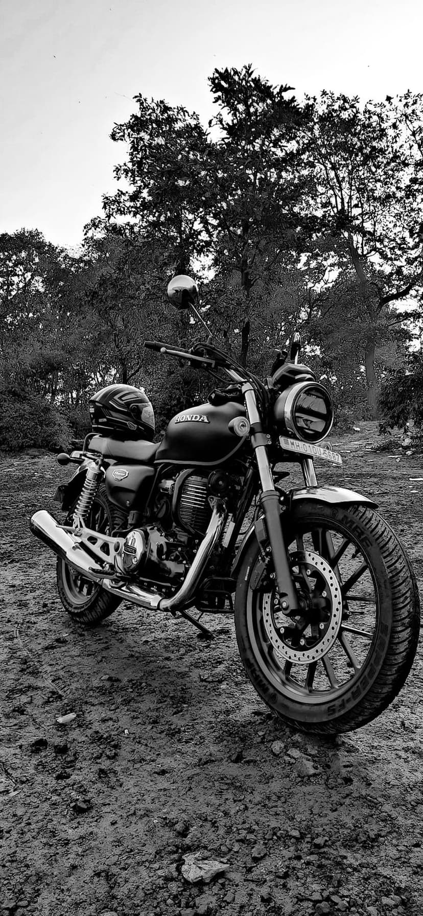 Honda motorcycle with a helmet on the seat parked in a dense forest with monochrome lighting and leafy trees.