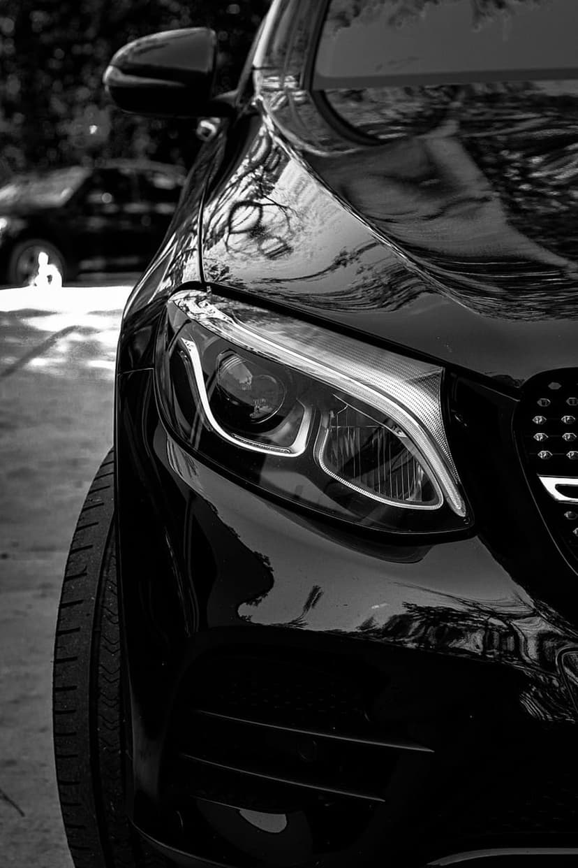 Mercedes-Benz headlight and chrome grille showing intricate reflections in a high-contrast monochrome style.
