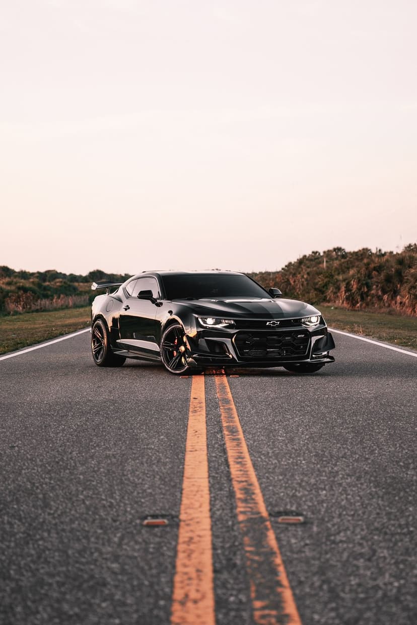 Black Chevrolet Camaro ZL1 on an asphalt road with yellow lines under a golden sunset sky during golden hour.