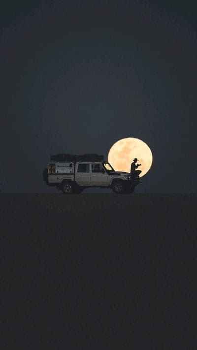 Lone figure silhouetted against full moon with off-road vehicle