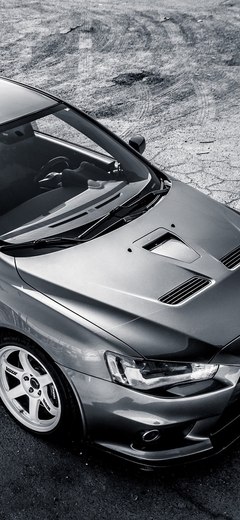 Grey Mitsubishi Lancer Evo X with white Volk wheels and vented hood parked on a textured dirt surface.