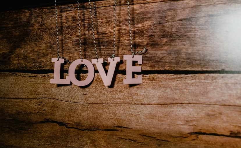Pink wooden letters spelling love hang by strings against a textured brown rustic wood plank background.