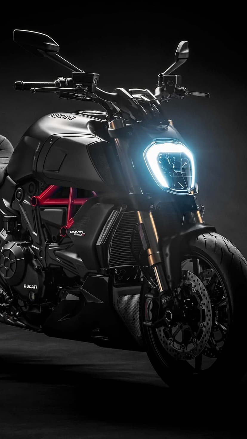 Ducati Diavel motorcycle with a glowing LED headlight, red trellis frame, and dual disc brakes in the dark.