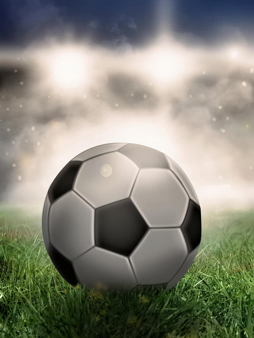 Soccer ball on green grass illuminated by bright stadium floodlights against a misty and dark night sky.