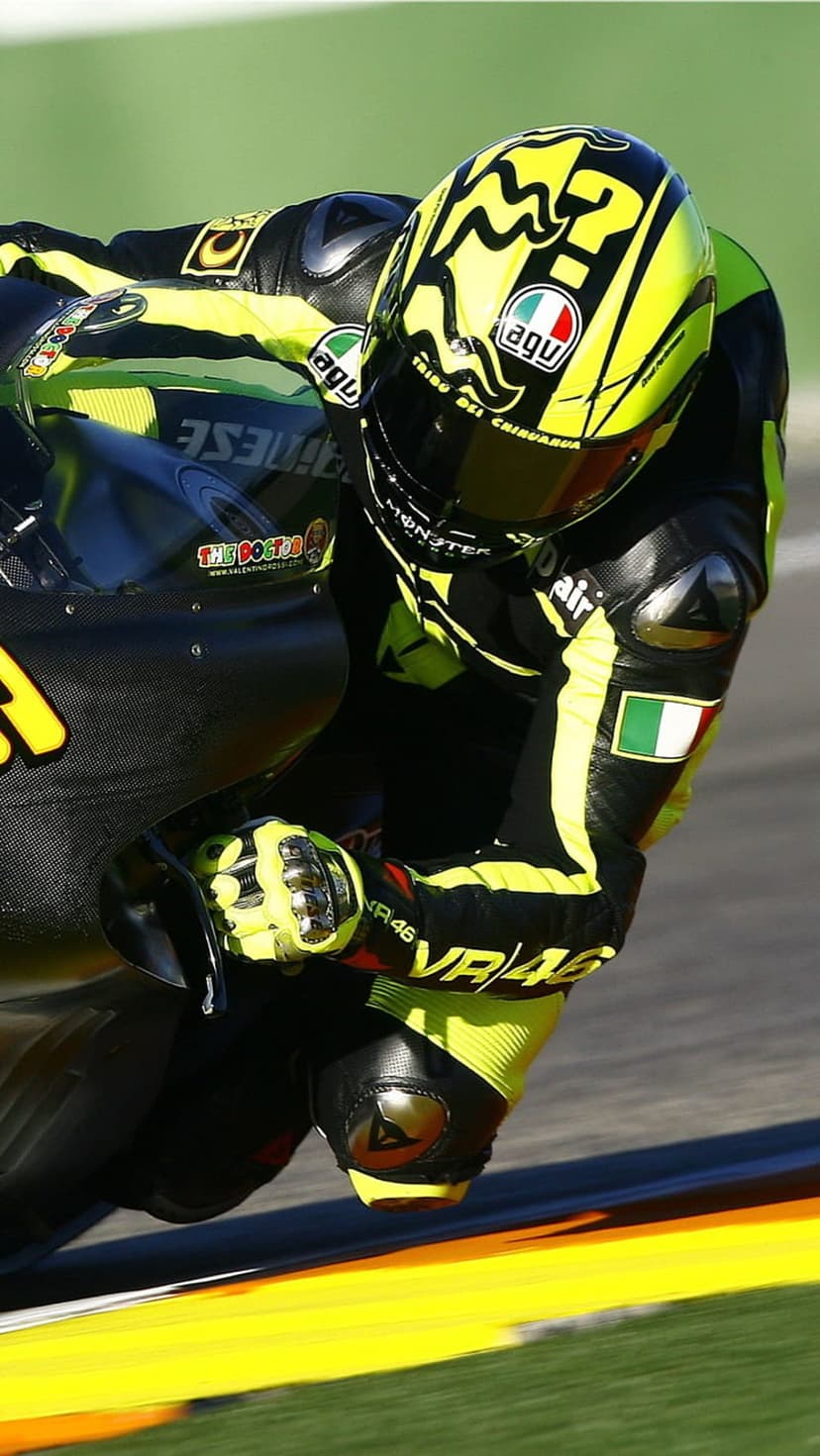 Valentino Rossi in yellow and black leathers leans a racing motorcycle into a sharp turn on a paved track.