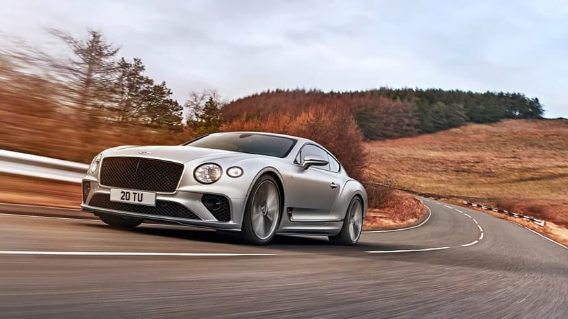 Silver Bentley Continental GT sports car speeding through a winding mountain road with motion blur.