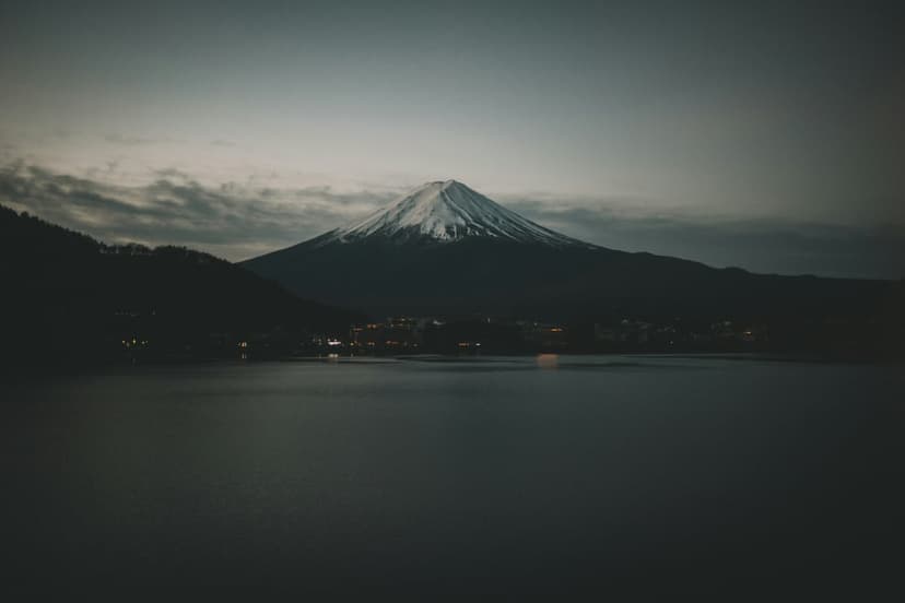 Mount Fuji with a snow-covered peak towers over a reflective lake during the purple and blue light of twilight.