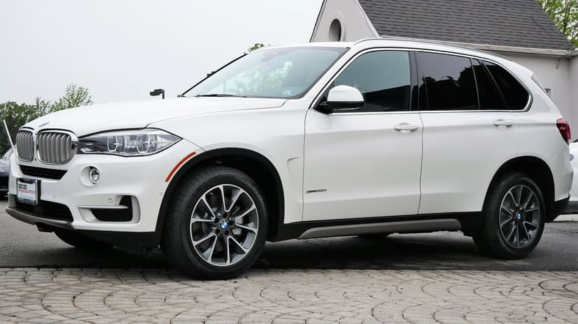 White BMW X5 luxury SUV parked on a circular stone driveway under soft daylight, featuring dark alloy wheels.