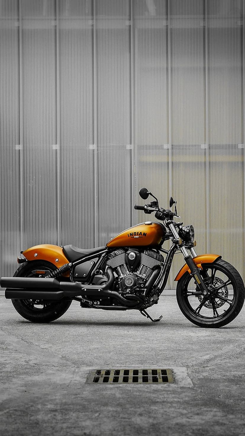 Orange Indian motorcycle with black exhaust pipes parked on concrete in front of a grey ribbed metal wall.