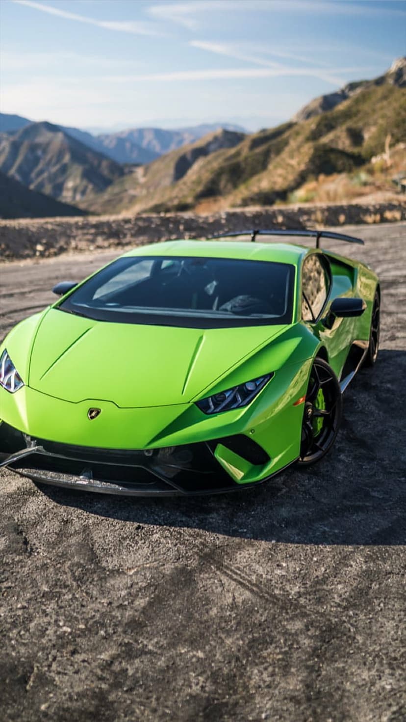 Lime green Lamborghini Huracan with a rear wing parked on a dirt road within a dramatic mountainous landscape.