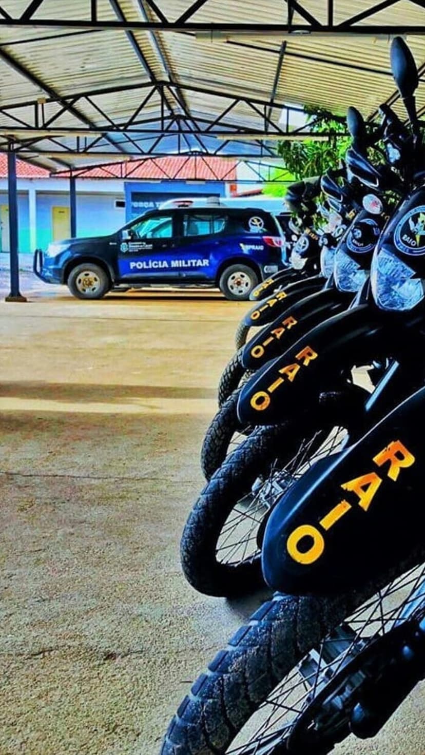 Brazilian police motorcycles with yellow lettering and a blue SUV parked in a line under a covered structure.