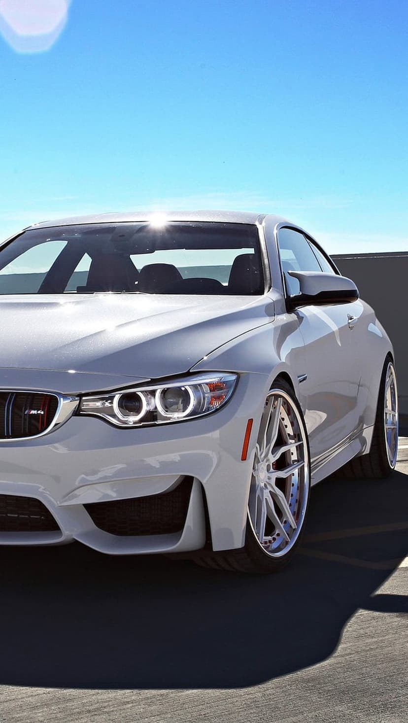 White BMW M4 coupe with silver wheels and aggressive front grille parked on asphalt under a bright blue sky.