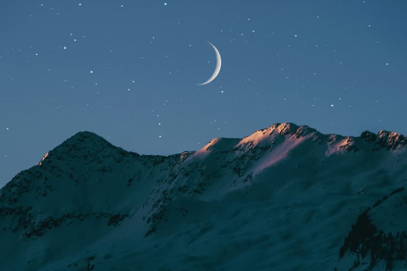 Crescent moon illuminates snow-dusted mountain peaks and a starry sky in this vertical alpine wilderness scene.