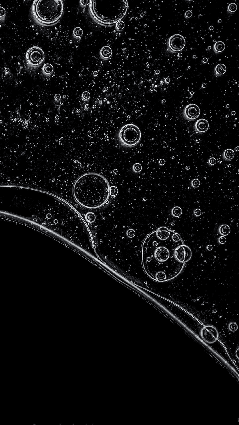 Spherical translucent bubbles with sharp highlights drift through a deep black liquid in a macro close-up view.