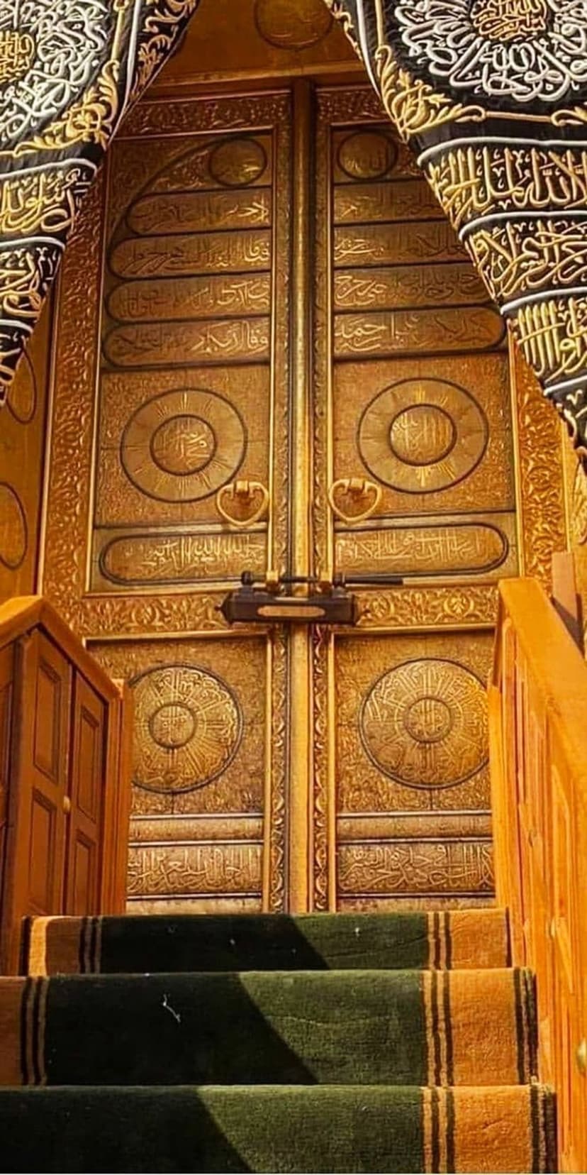 Golden Kaaba doors with Arabic calligraphy above green carpeted stairs lead into the sacred mosque entrance.