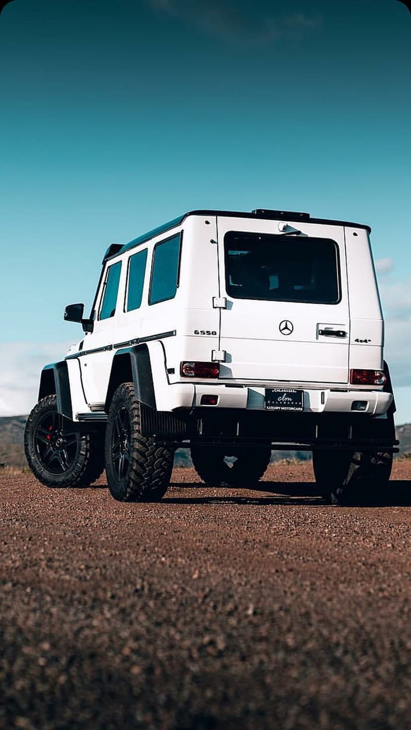 White Mercedes G-Wagen 6550 with aggressive tires on rocky desert ground under a clear blue sky.