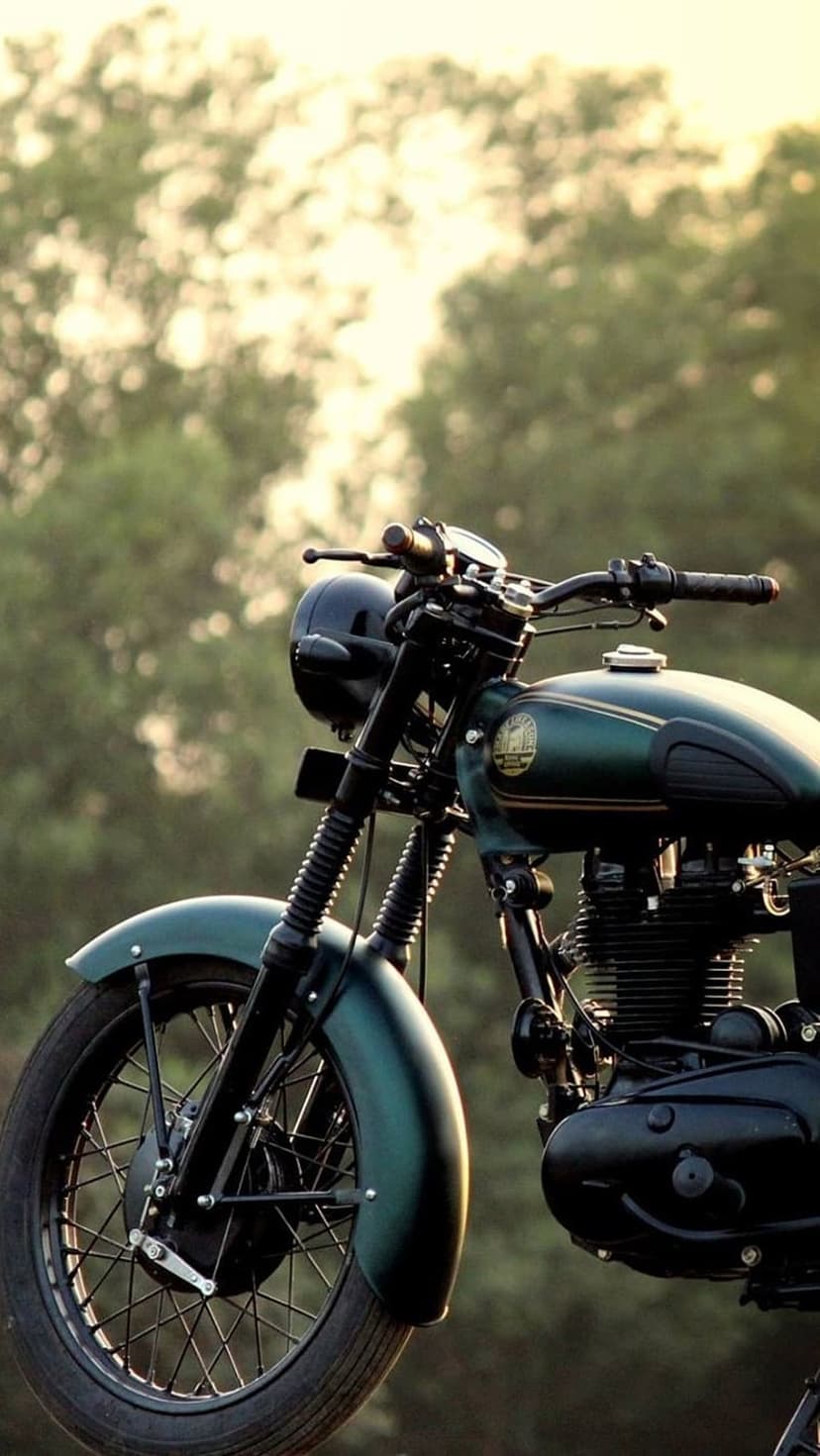 Vintage Royal Enfield motorcycle in forest green parked outdoors with sunlight reflecting off chrome accents.
