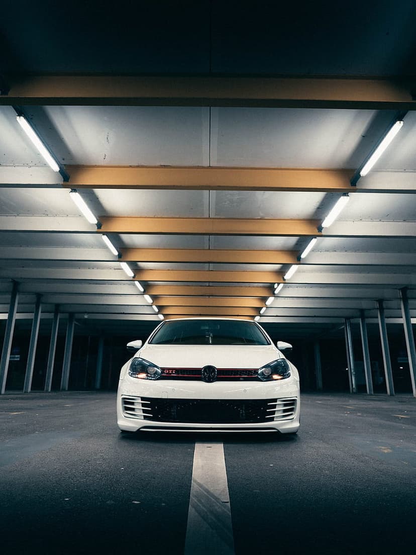 White Volkswagen Golf GTI parked in a concrete underground garage with moody fluorescent lighting and dark shadows.