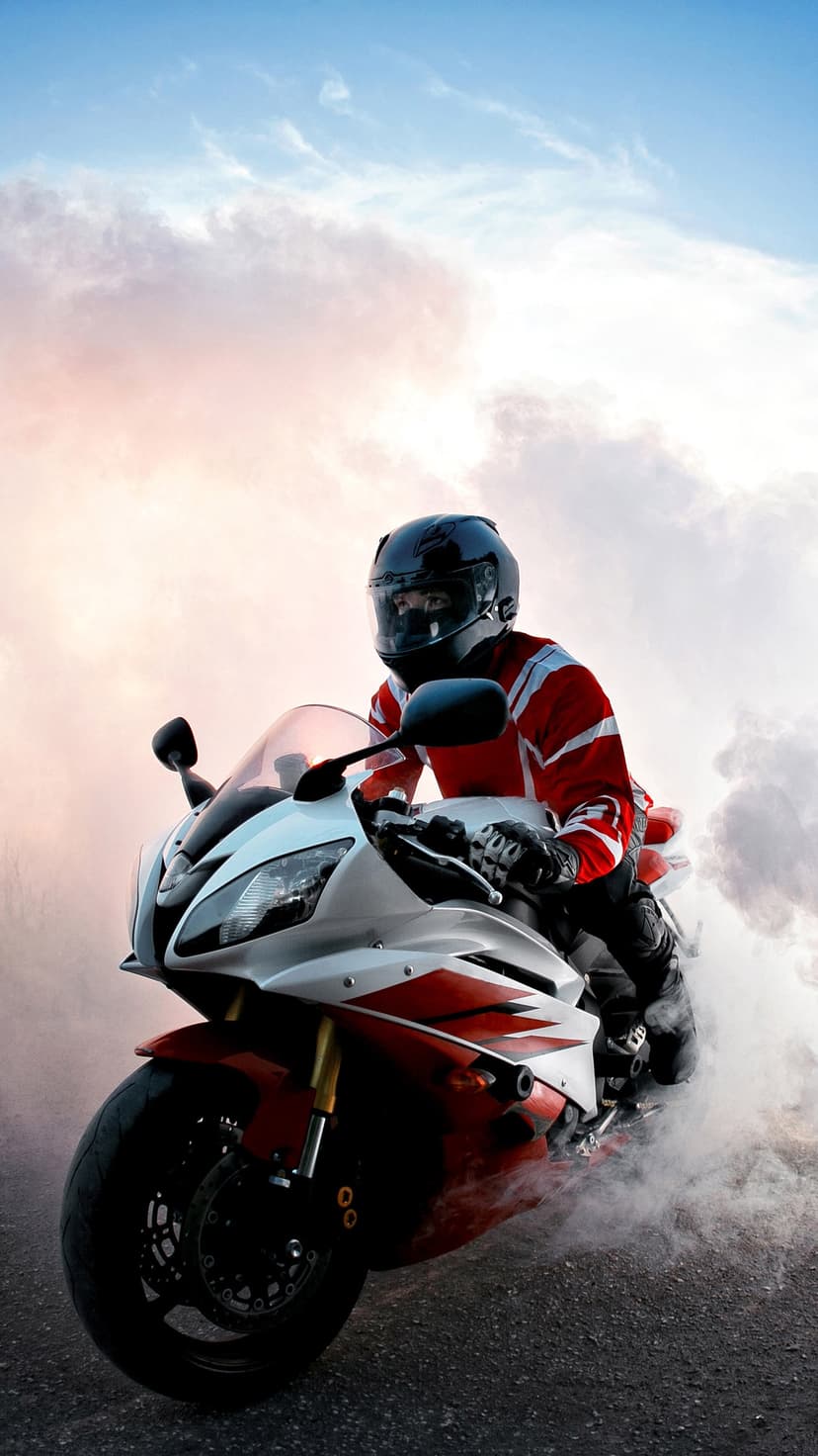 Motorcyclist in a red suit performs a smoky burnout on a sportbike during a vibrant golden hour sunset.