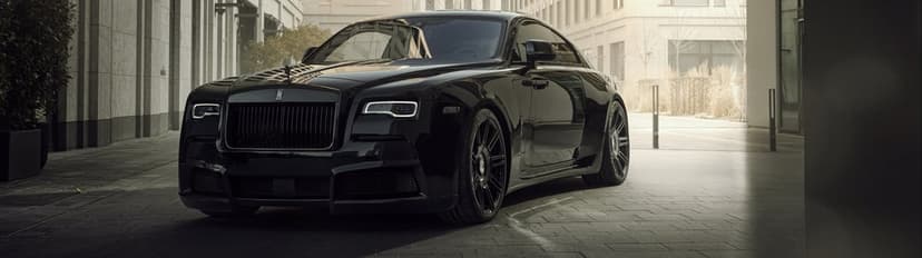 Front view of a black Rolls-Royce Wraith coupe parked in a sunlit urban alley with modern stone buildings.