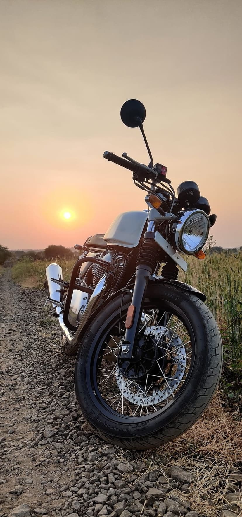 Royal Enfield Interceptor 650 motorcycle parked on a dirt road during a vivid golden hour sunset with chrome accents.