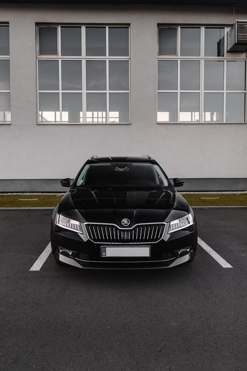 Black Skoda station wagon with a chrome grille parked in front of a modern building with segmented windows.