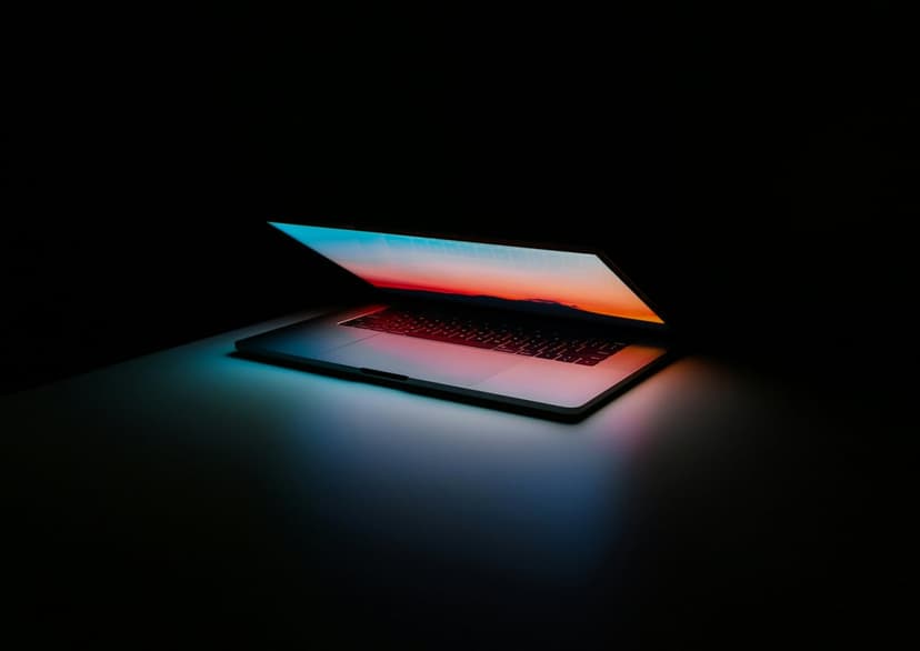 Glowing laptop displaying a sunset casts warm light on a keyboard and dark desk in a minimalist setting.