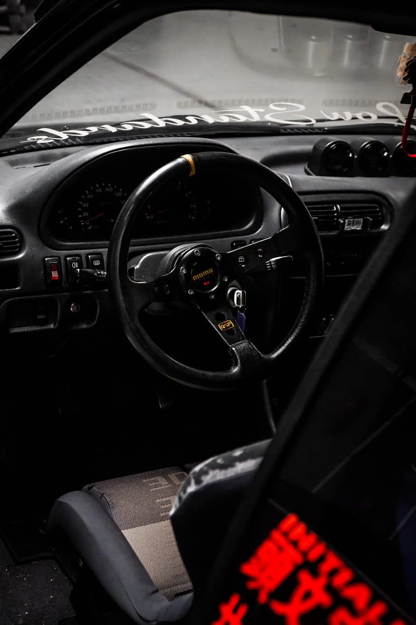 Momo steering wheel and racing bucket seat inside a modified car cockpit with a Low Standards windshield sticker.