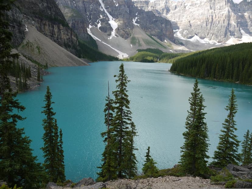Moraine Lake shines with turquoise glacial water beneath snow-capped Canadian Rocky Mountains and evergreen trees.