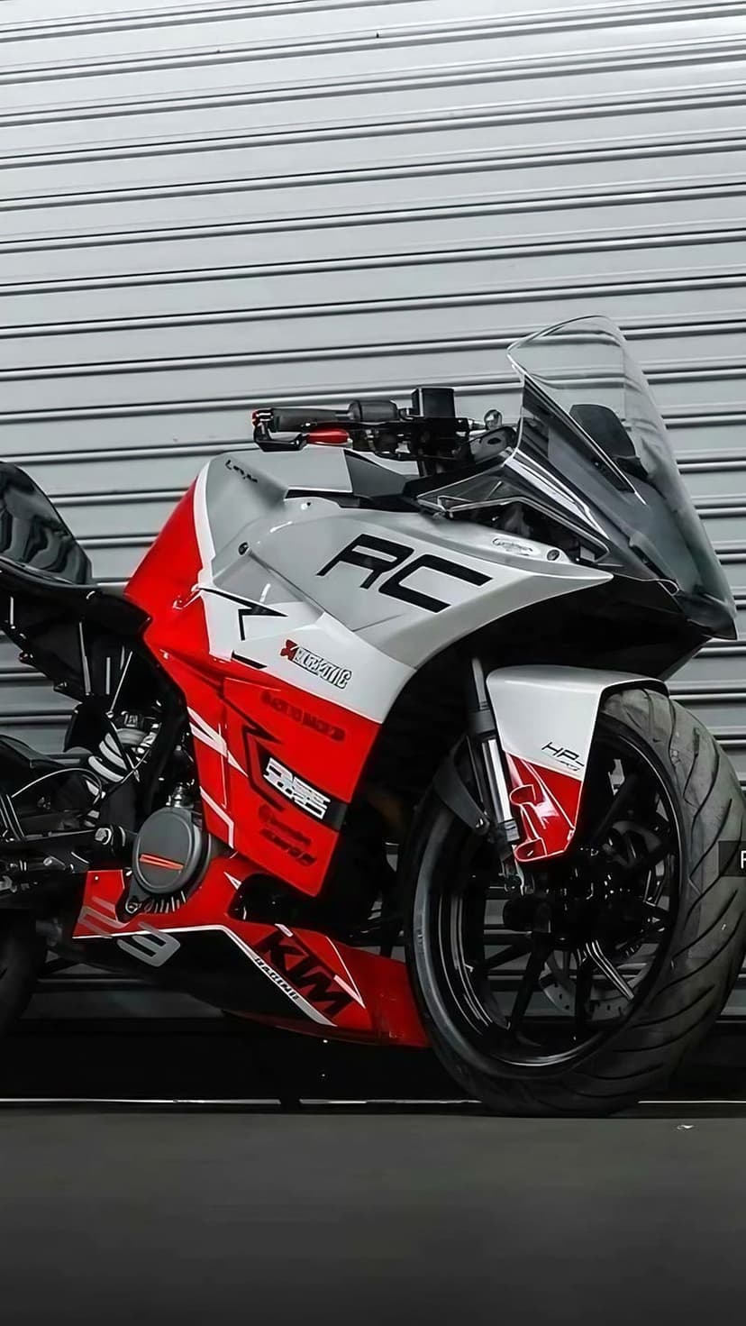 KTM RC motorcycle with red and silver fairings and Akrapovič branding against a corrugated metal wall.