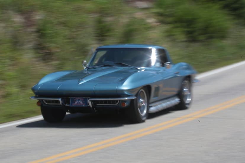Teal Corvette Stingray with chrome accents driving on a highway with yellow lines and blurred greenery.