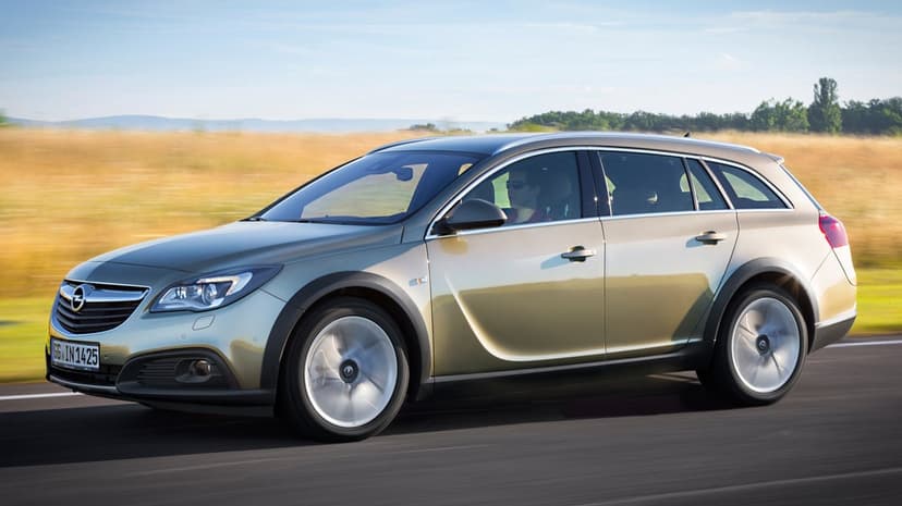 Opel Insignia Country Tourer driving at speed on a road with motion blurred wheels and a golden field background.