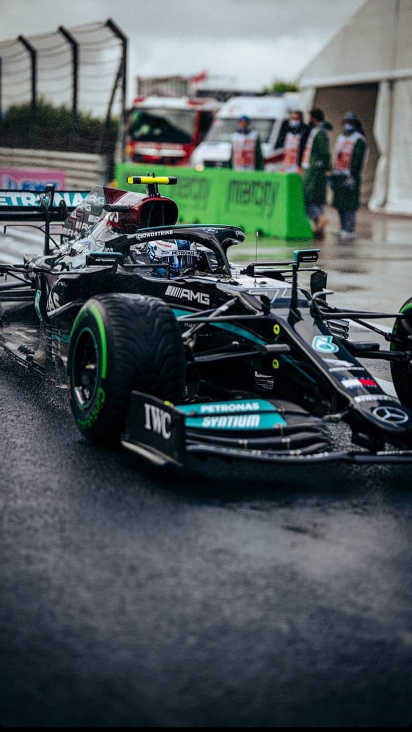 Valtteri Bottas drives a black Mercedes F1 car on a rain-soaked track with visible water spray and sponsor logos.